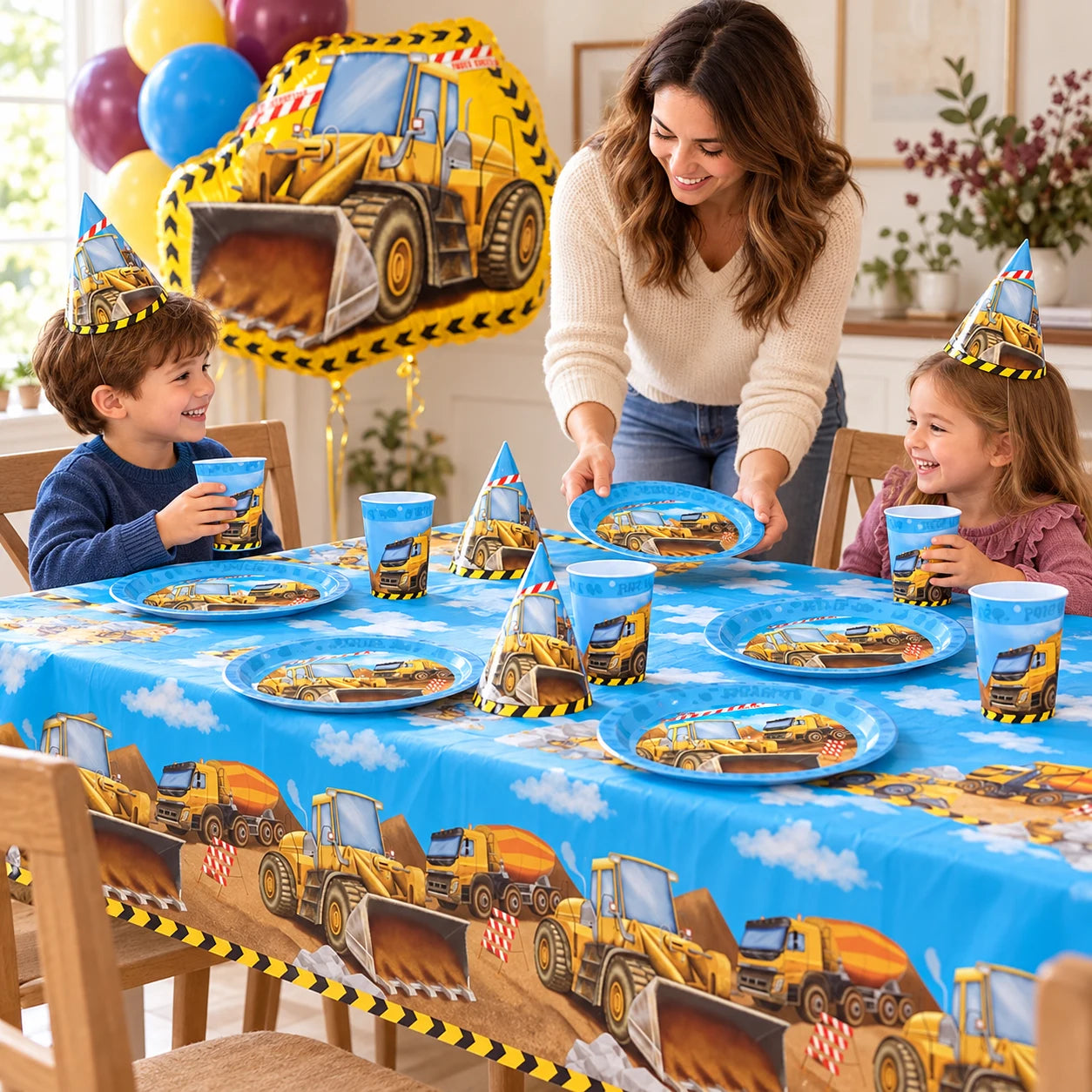 Family setting a construction birthday table with the blue vehicle tablecover, reusable plates, cups, hats and dozer balloon sold by Shimmer & Confetti